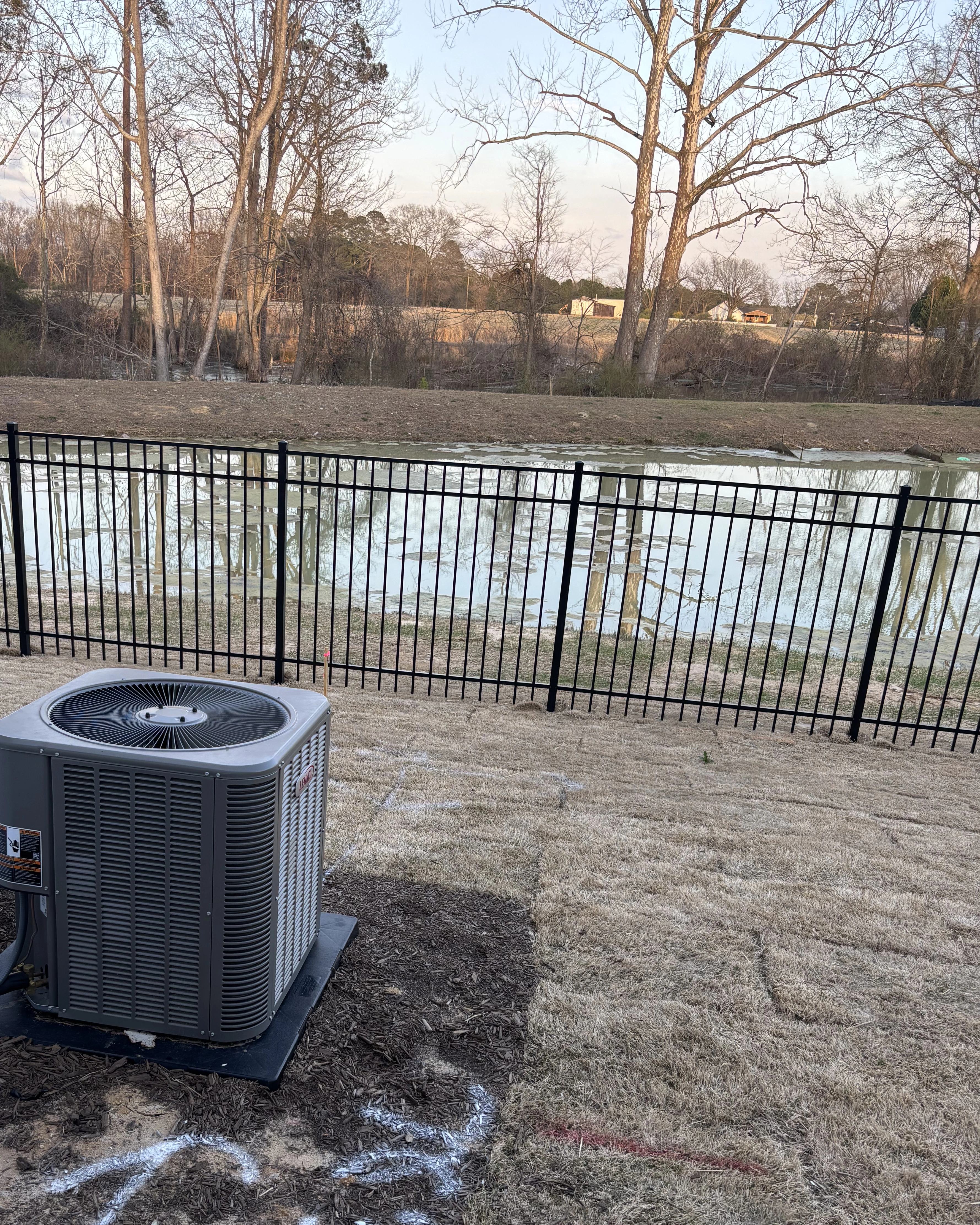 Black aluminum fence installed beside a backyard pond overlooking wooded land.